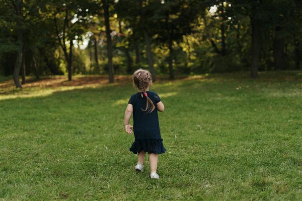 دختر کوچک شاد در حال دویدن روی چمن سبز