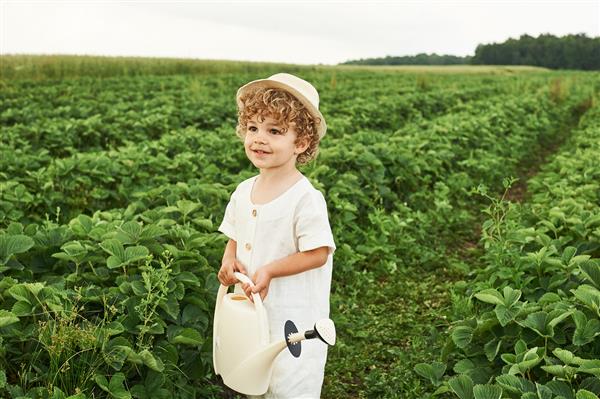 یک پسر بچه فرفری با کلاه سفید و لباس کتانی در مزرعه