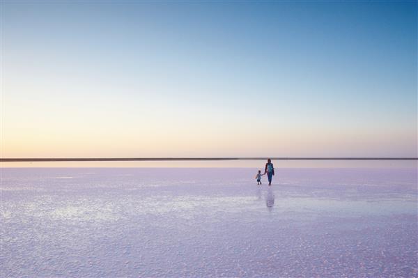 مادر و کودک در حال راه رفتن بر روی نمک و آب نمک دریاچه صورتی