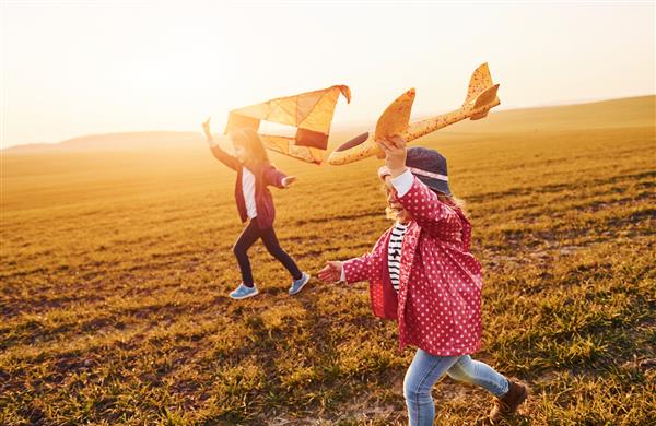 دو دوست دختر کوچک با بادبادک و هواپیمای اسباب بازی در روز آفتابی در زمین خوش می گذرانند