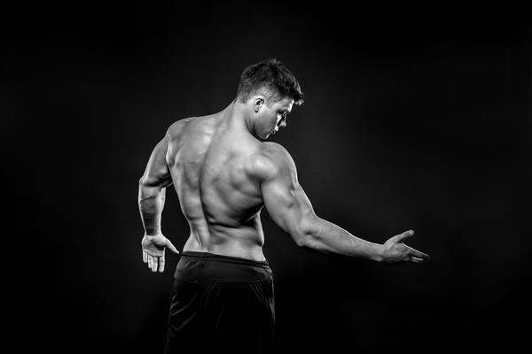 ورزشکار جوان که با لباس مشکی در استودیو عکس می گیرد تناسب اندام بدنسازی سیاه و سفید