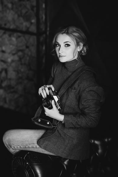 عکاس بلوند دختر زیبا با کت و شلوار سخت دوربین قدیمی را در دستان خود دارد
