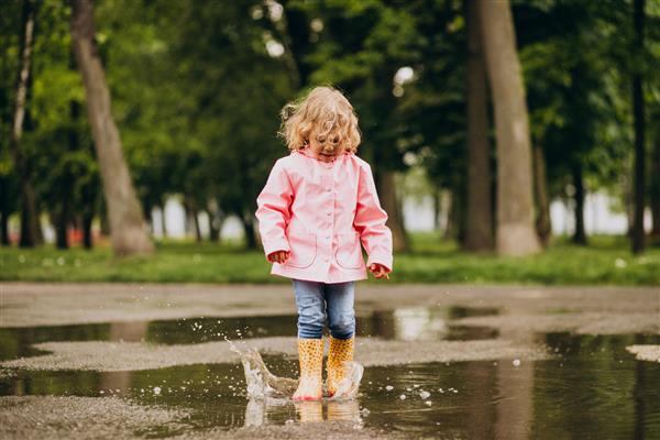 پریدن دختر کوچک ناز در آب و هوای بارانی به گودال