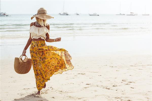 دختری با دامن گلدار که با پای برهنه در ساحل دریا تایلند پوکت راه می‌رود