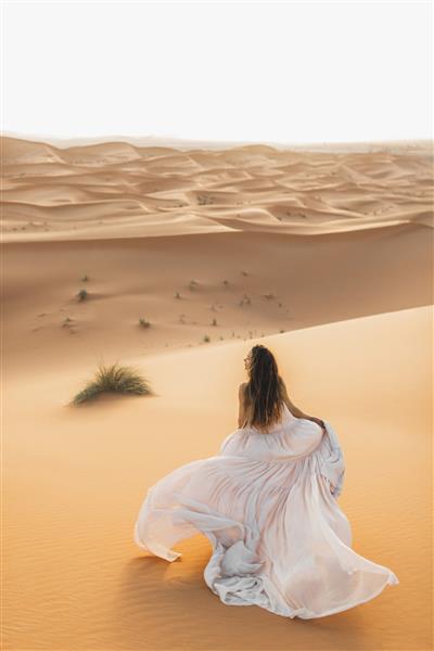 پرتره زن عروس با لباس عروس شگفت انگیز در صحرای صحرا مراکش نور گرم عصر رنگ پاستلی زیبا تپه های شنی در افق نمای از پشت