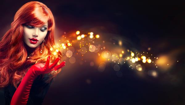 زن زیبای با جادوی جرقه های طلایی در دستش موهای موج دار قرمز بلند