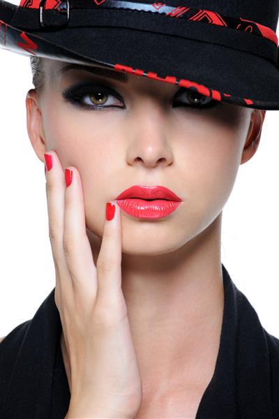 چهره نزدیک زن زیبا با لب های قرمز روشن و ناخن های دست در کلاه مد