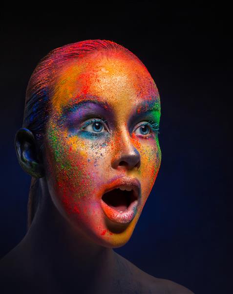 آرایش خلاقانه هنری رنگ های مقدس مدل مد جوان متعجب احساسی با ترکیب رنگارنگ روشن روی صورتش