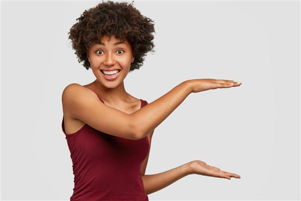زن جوان سیاه‌پوست شاد با حالت چهره خوشحال قد چیزی را نشان می‌دهد