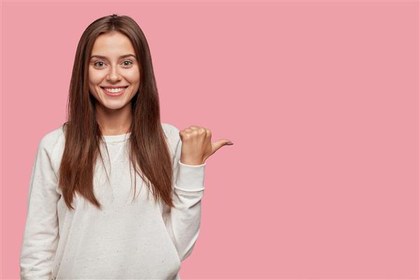 زن جوان اروپایی شاد و مثبت با موهای تیره لبخند پهن و درخشان با انگشت شست کنار