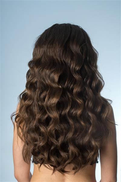 دختری با موهای مجعد بلند در استودیو روی خاکستری