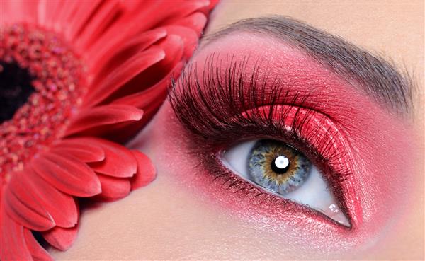 چشم زن مد با آرایش قرمز و مژه های مصنوعی بلند - گل در پس زمینه