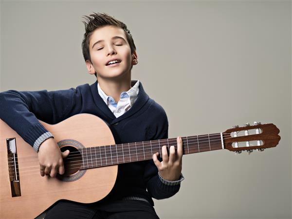 پسر خوشحال در حال نواختن با لذت روی گیتار آکوستیک