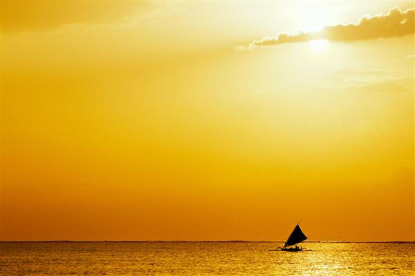 منظره دریایی با غروب طلایی و یک قایق بادبانی در وسط اقیانوس