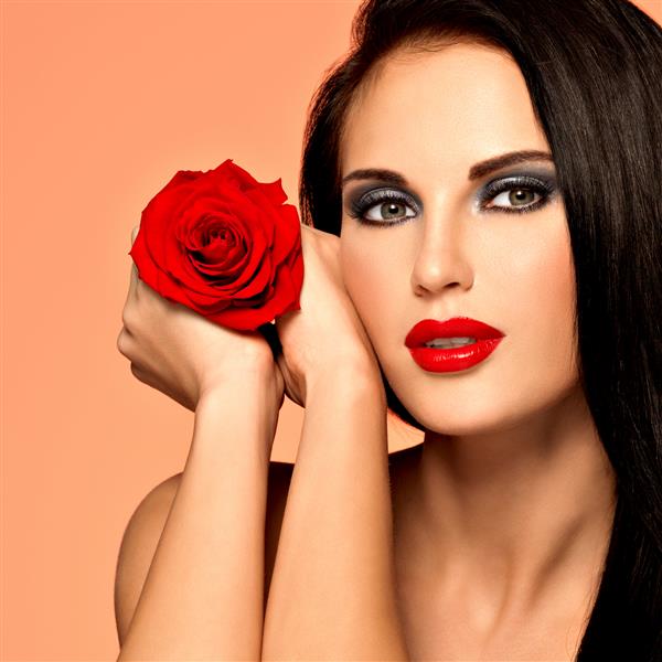 پرتره زن زیبای زیبا با آرایش مد روشن گل رز قرمز را نگه می دارد