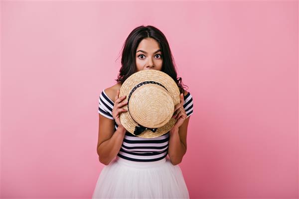 زن برنزه برنزه ای که صورتش را در کنار کلاه حصیری پنهان کرده است پرتره سرپوشیده بانوی لاتین شایان ستایش که بازیگوش ژست گرفته است
