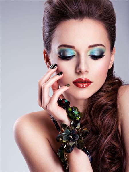 صورت زن زیبا با آرایش سبز مد و جواهرات در دست