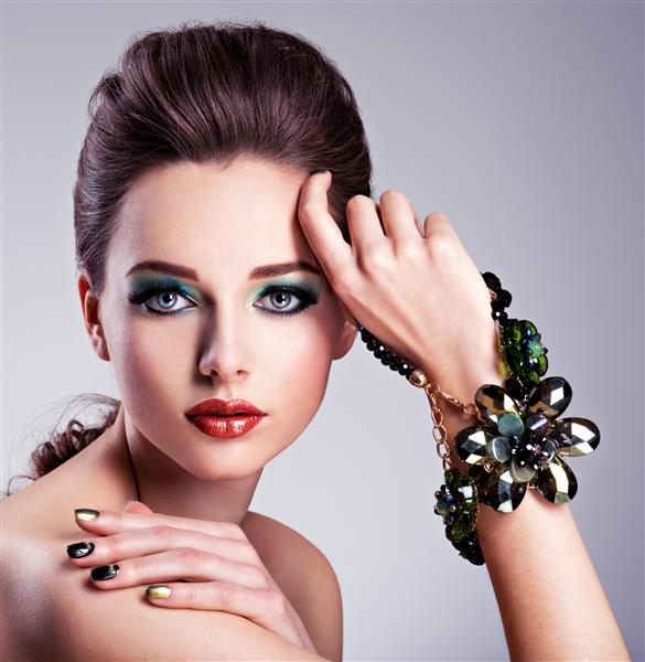 صورت زن زیبا با آرایش سبز مد و جواهرات در دست