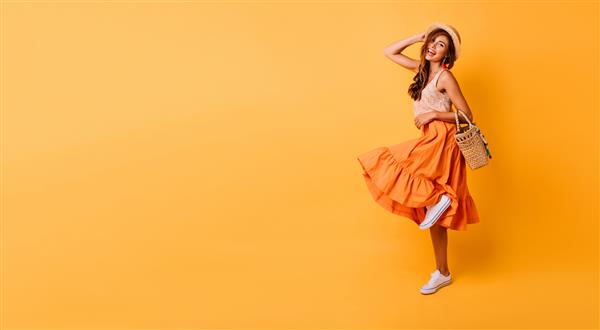 زن باشکوه با دامن بلند روشن در حال رقصیدن در استودیو مدل زن با الهام از بی خیالی که با لذت روی رنگ زرد ژست می گیرد