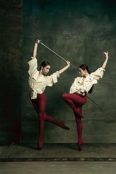 پرشور دو رقصنده زن جوان مانند دوئل با شمشیر روی دیوار سبز تیره رقص مدل های قفقازی با هم باله و مفهوم رقص معاصر