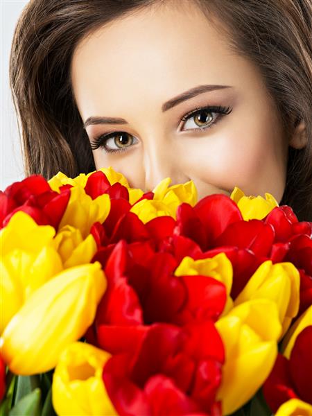 چشمان زیبای زن در میان گل ها پرتره دختری جذاب که صورت را با لاله های قرمز و زرد پوشانده است