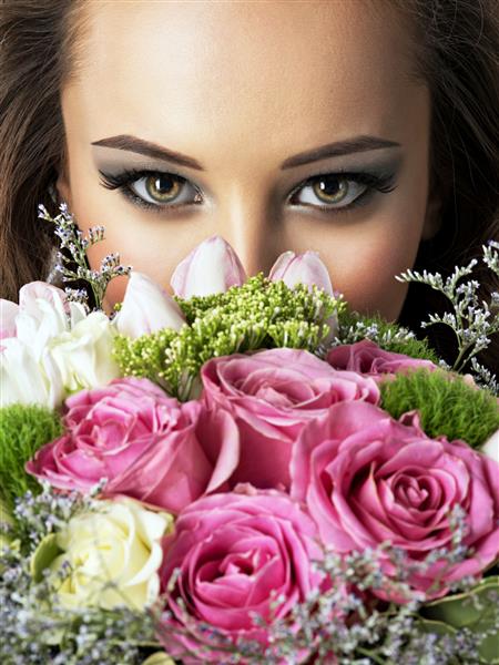 چهره نزدیک دختر زیبا با گل زن جوان جذاب دسته گل های بهاری را در دست گرفته است