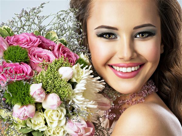 پرتره نزدیک دختر شاد زیبا با گل در دست زن جوان جذاب دسته گل های بهاری را در دست گرفته است
