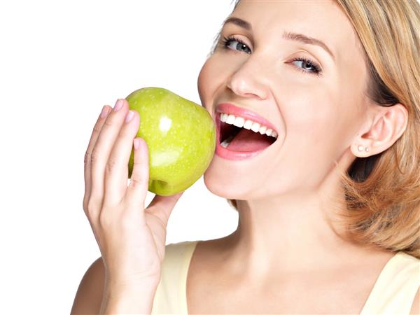 زن جوان زیبا در حال گاز گرفتن یک سیب تازه رسیده - روی دیوار سفید