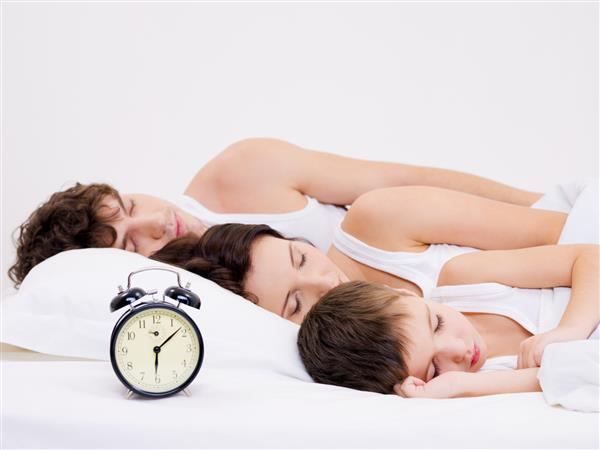 سه نفر از خانواده جوان در حال خواب با ساعت زنگ دار نزدیک سرشان