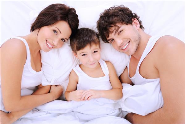 پرتره با زاویه بالا از والدین خندان شاد با پسر کوچکی که روی تخت دراز کشیده است