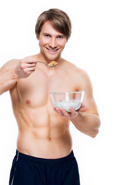 پرتره یک مرد عضلانی جذاب جوان در حال خوردن تکه های با شیر - جدا شده روی دیوار سفید