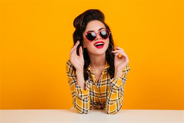 دختر پیناپ وجدی که با عینک های قلبی شکل ژست گرفته است عکس استودیویی از زن زیبا رویایی با پیراهن چهارخانه