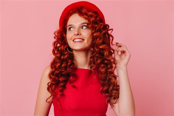 دختر جذاب مو قرمز با لبخند به دور نگاه می کند زن با کلاه و تاپ قرمز موها را لمس می کند