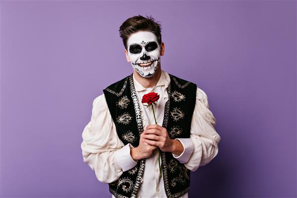 مردی با موهای تیره با لبخند زیبا با خلق و خوی عالی روی دیوار جدا شده ژست گرفته است عکس مکزیکی با چهره هنری و گل رز در دستانش