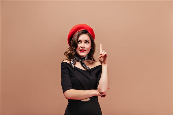 خانم فرفری با لب‌های قرمز متفکرانه به بالا نگاه می‌کند و انگشت اشاره را به سمت بالا نشان می‌دهد پرتره زنی با کلاه بلند و لباس مشکی