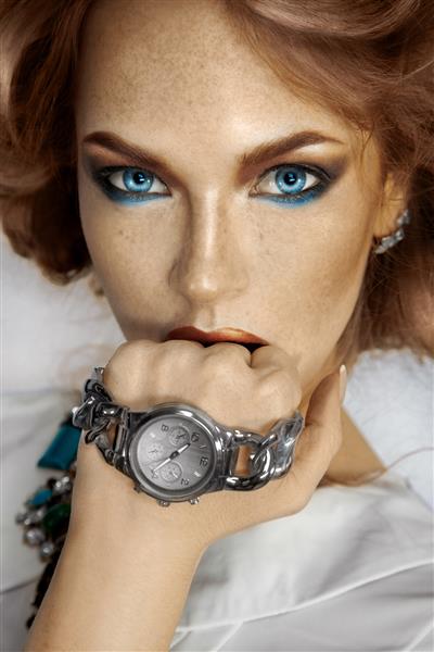 زن زیبا با ساعت در دست که به دوربین نگاه می کند