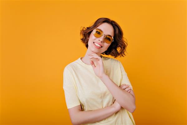 دختر پریده رنگ پریده با عینک آفتابی قدیمی که با لبخند ژست گرفته است عکس داخلی از مدل زن زرق و برق دار با لباس زرد روشن