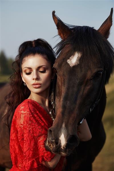 دختری با لباس بلند نزدیک اسبی ایستاده است زنی زیبا در پاییز در مزرعه ای اسبی را نوازش می کند و افسار را نگه می دارد زندگی روستایی و مد اسب نجیب