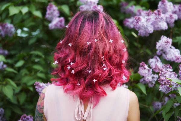 رنگ آمیزی مو در موهای دخترانه صورتی قرمز روشن با گل های یاسی رنگ اشباع روشن مو زنی که در شاخه های یاسی ژست گرفته است