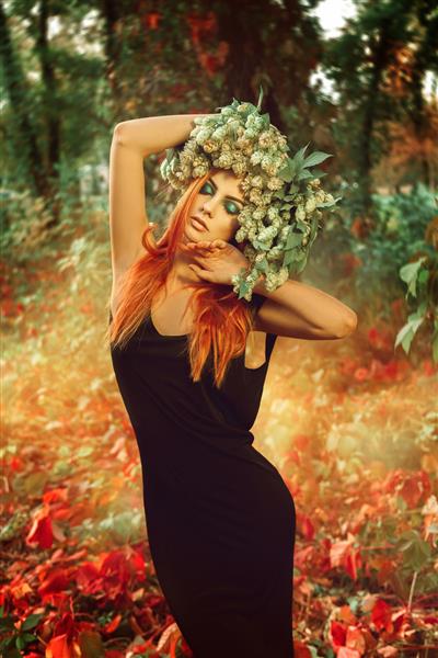 خانم جوان لاغر و خیره کننده با موهای قرمز و تاج گل رازک روی سر در فضای باز