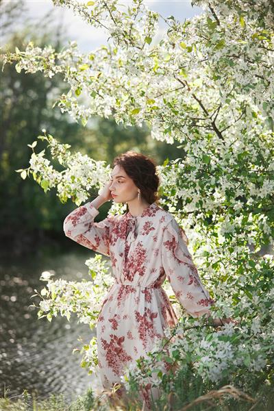 زن زیبای عاشقانه در شاخه های درخت سیب شکوفه ایستاده است پرتره بهاری دختر در گل درخت سیب
