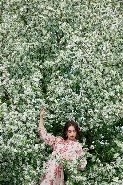 زن با آرایش طبیعی لوازم آرایشی گلدار برای پوست صورت دختری که در شاخه های گل درخت سیب شکوفه در بهار ژست گرفته است