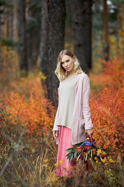 دختری که در جنگل پاییزی قدم می زند یک دسته گل زیبای بزرگ در دستان یک زن دختر در چمن قرمز زرد طبیعت پاییزی ایستاده است