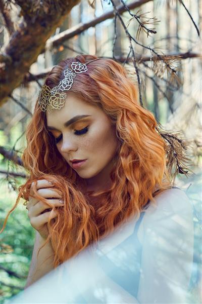 دختر زیبای مو قرمز نروژی با چشمان درشت و کک و مک صورت در جنگل پرتره نزدیک زن مو قرمز در طبیعت ظاهر اسرارآمیز افسانه ای موهای قرمز مواج بلند در زیر نور خورشید مراقبت از مو