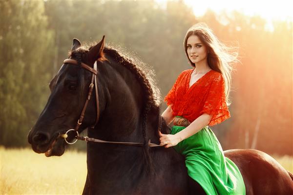دختر کولی در تابستان سوار بر اسب در مزرعه ای می شود زنی با موهای بلند اسبی را که در میان چمن‌های سبز ایستاده است نوازش می‌کند
