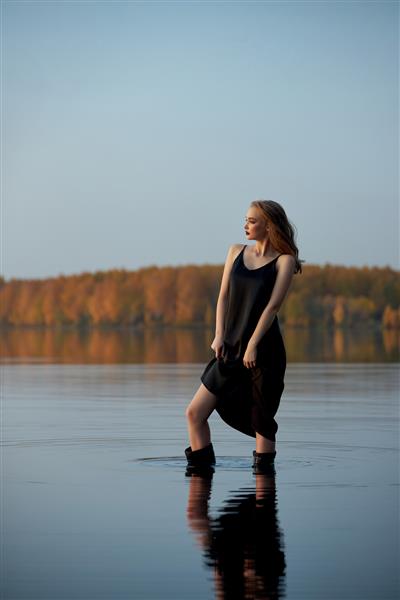 زن زیبای زیبا در آب در کنار حوض در زیر پرتوهای غروب خورشید ایستاده است