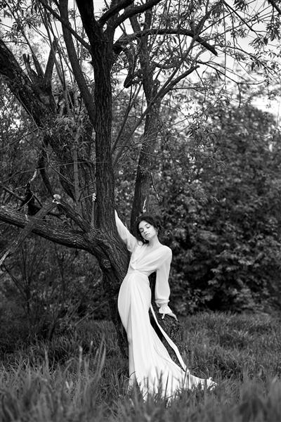 زن جوان وابسته به عشق شهوانی با لباس سفید بلند در پارکی بهاری نزدیک رودخانه قدم می زند ژست گرفتن سبزه زیبا در طبیعت