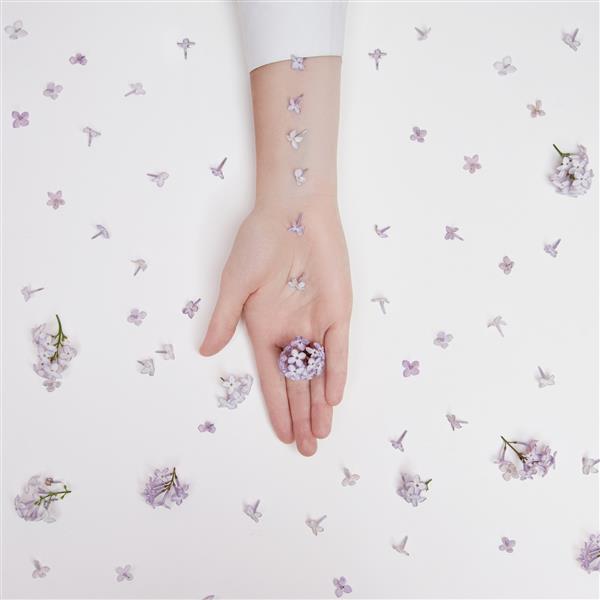 گل های سوسن بهاری در دستان زنی که روی میز سفید دراز کشیده است لوازم آرایشی طبیعی دست ضد چروک دست زیبایی طبیعی یک زن