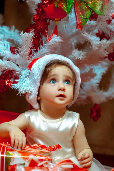 کودک کوچک هدیه زیر درخت کریسمس باز می شود خلق و خوی کریسمس سال نو