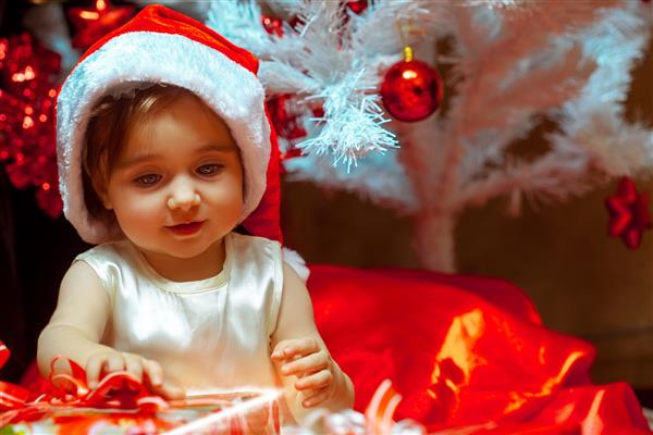 دختر کوچک هدیه را زیر درخت کریسمس باز می کند خلق و خوی کریسمس سال نو